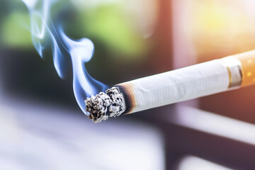 A glowing cigarette rests in focus, with wisps of smoke elegantly rising into the air, set against a warm, softly blurred outdoor background revealing hints of nature. Generative AI