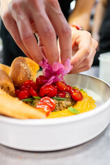 A close-up shot of a hand garnishing a dish with red cherry tomatoes and purple flowers, showcasing a vibrant and colorful culinary presentation. Perfect for food photography