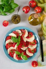 Italian Caprese salad with sliced tomatoes, mozzarella cheese, basil and olive oil on blue plate on light gray background. Top view