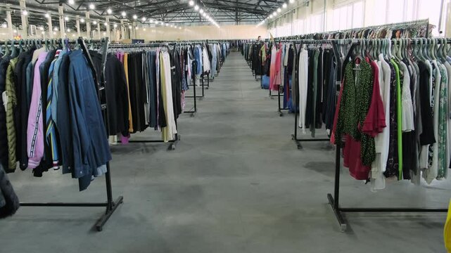 Large second-hand clothing store interior with numerous racks of diverse clothing under bright industrial lights.
