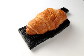 Crispy hot croissant on a black rectangular wooden board on a white background