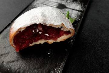 An appetizing donut with strawberries sprinkled with powdered sugar on a black rectangular plate on a gray background