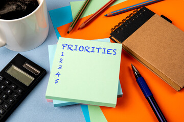 Priorities List. Notepad with text, coffee mug and calculator and stationery on office table