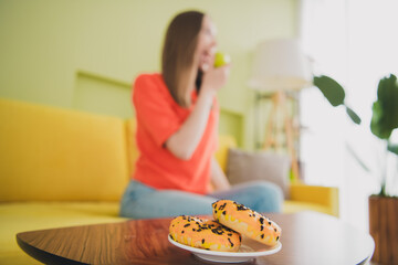 Photo of lovely young girl eat apple avoid donut diet dressed orange garment spacious house spring indoors room