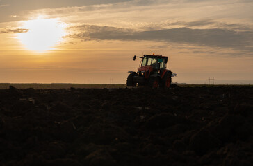 Obraz premium Tractor on the field during sunset.