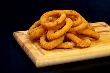 Onion rings fried on a wooden board, on a black background. Beer snack.