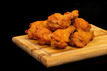 Chicken drumsticks fried on a wooden board, on a black background. Beer snack.