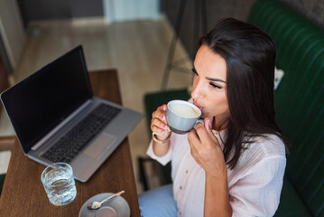 Beautiful businesswoman drinking coffee and working on laptop in a cafe