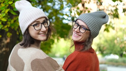 Two women friends or sisters hugging outdoors in autumn park