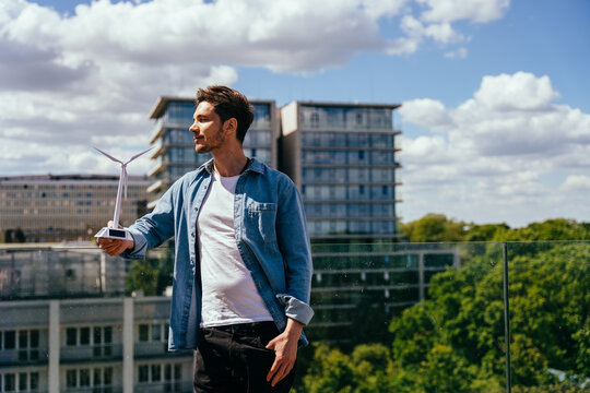 Confident man holding wind turbine model on rooftop