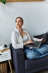 Obraz premium A young woman casually dressed sits comfortably on her couch, working intently on her laptop.