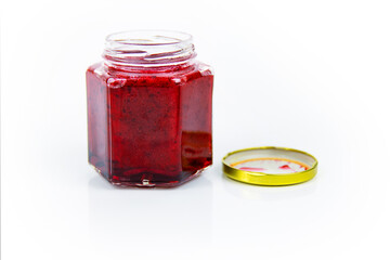 An open hexagonal glass jar of homemade red currant berry or cranberry jam with a gold lid beside...