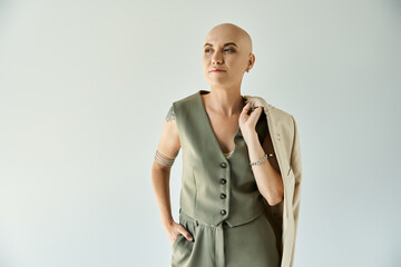 A young bald woman with alopecia poses gracefully, dressed in a stylish outfit, exuding confidence.