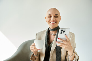 A joyful bald woman sips tea and engages with her phone, radiating confidence and warmth.