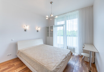 Wide Angle of Home Bedroom Interiom. King Size Double Bed and Windows, Door to Balcony in Background. White Walls. Family Home. Windows And Curtains. Desk and Chair