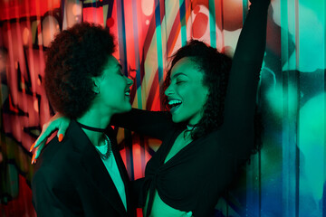 Two women share a joyful moment, celebrating friendship in a vibrant setting.