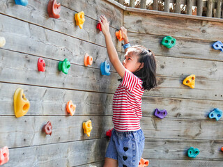 Children play outdoors on a wooden playground in a park. Happy girl playing on wooden climbing wall...