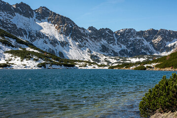 Obraz premium An unparalleled view of a crystal-clear lake in the Valley of Five Ponds, Tatra Mountains, Poland, reveals stunning alpine beauty, surrounded by rugged peaks and lush greenery