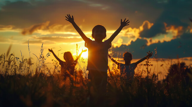 Silhouette back view of a group of refugee kids playing at sunset. Children raising hands in worship. Hope, freedom, diverse faith, praise, World Refugee Day, adoption concept.