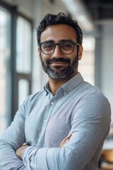 Naklejka premium A confident bearded man with glasses smiling in a modern office setting, dressed professionally for work.