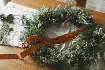 Making stylish Christmas rustic wreath. Wreath with fir and evergreen branches, ribbon, twine,...