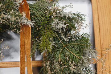 Stylish christmas rustic wreath with ribbon hanging on wooden doors, close up. Modern farmhouse entrance decoration for winter holiday. Merry Christmas and Happy holidays