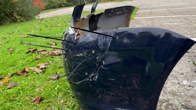 Damaged car bumper secured with zip ties after front-end collision. Improvised repair with duct-taped headlight and scattered road debris &ndash; temporary fix after accident impact
