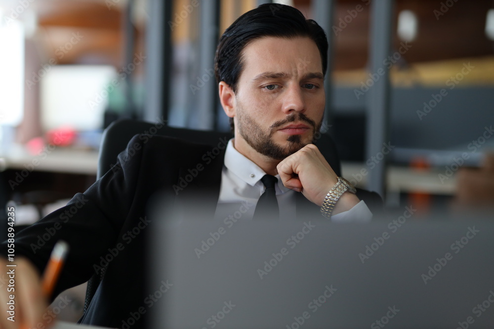 Poster a man in a suit is sitting at a desk with a computer monitor in front of him. he is wearing a watch 