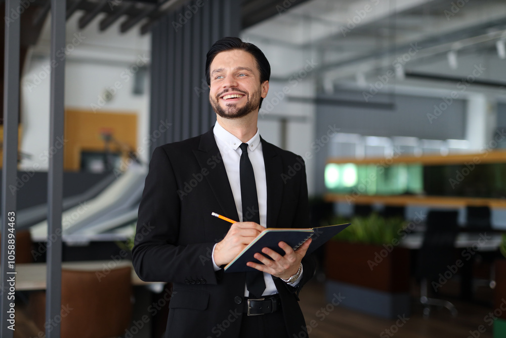 Poster a man in a suit is smiling and holding a pen and a notebook. he is happy and focused on writing some
