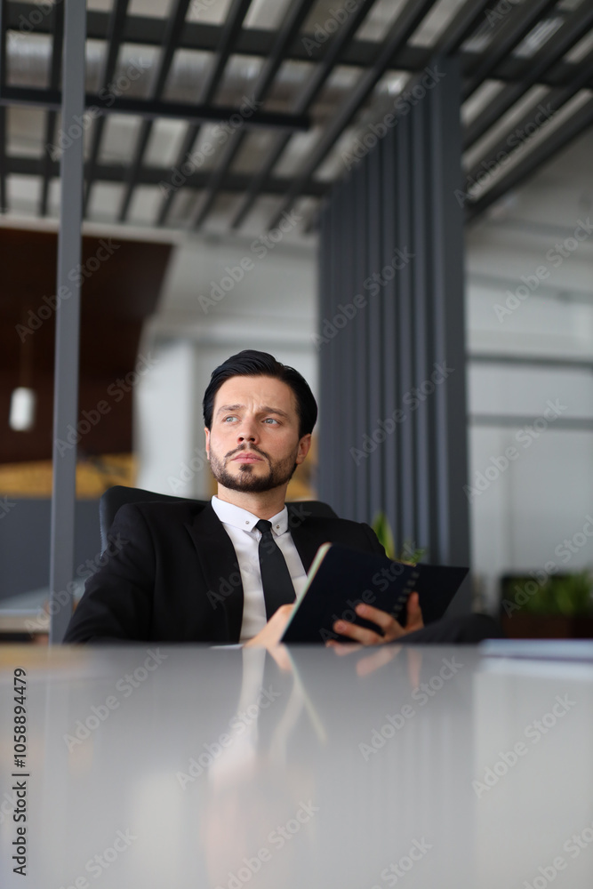Aufkleber a man in a suit is sitting at a desk with a book in front of him. he is focused on the book, possibl