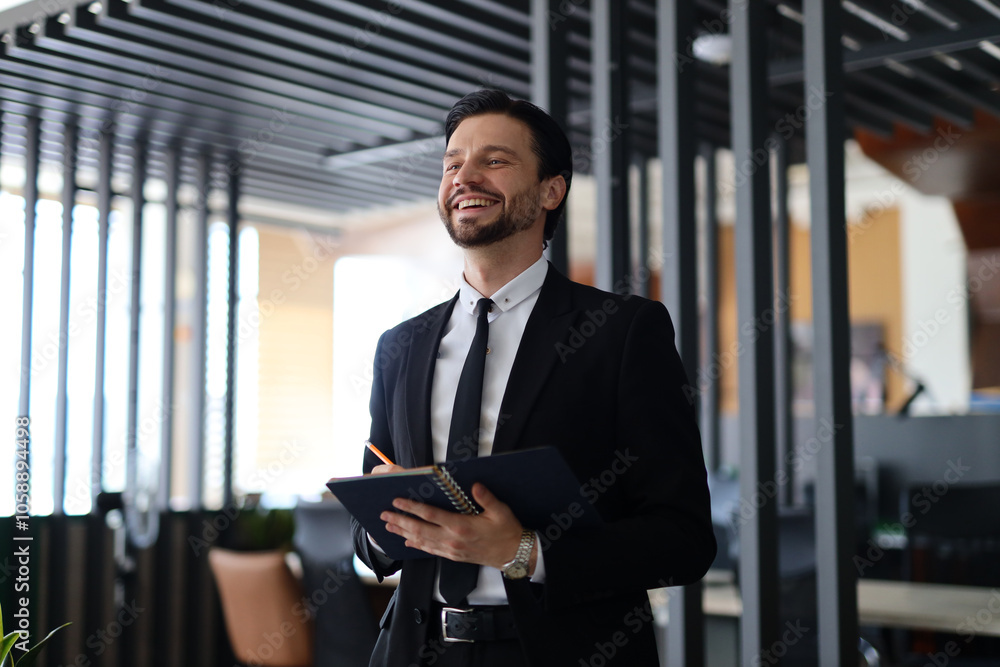 Poster a man in a suit is smiling and holding a notebook and a pen. he is happy and content