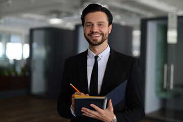 Fototapeta premium A man in a suit is smiling and holding a pen and a notebook. He is a businessman or a professional