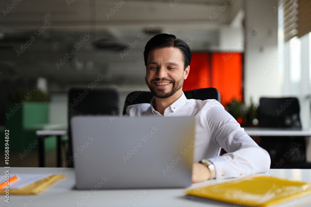 Poster a man is sitting at a desk with a laptop open in front of him. he is smiling and he is enjoying his 