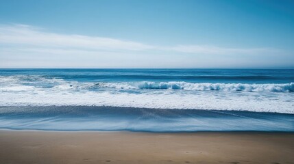 Wide canvas captures the serene beauty of expansive ocean blues, with impending white waves approaching a sandy shore, offering excellent photo style copy space for design.
