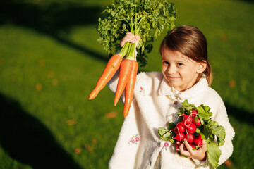 little girl farmer with vegetables and pumpkin on the background of green grass and vegetable garden. healthy eating concept.