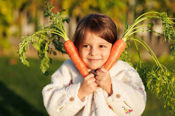 little girl farmer with vegetables and pumpkin on the background of green grass and vegetable garden. healthy eating concept.