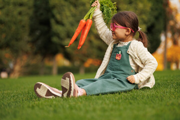 little girl farmer with vegetables and pumpkin on the background of green grass and vegetable garden. healthy eating concept.