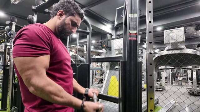 Close-Up Slow-Motion,Low-Angle View of Man with Big Biceps,Visible Veins Performing Cable Bicep Curl While Standing on Machine in Gym, Wearing a Watch on One Arm,with Background People Working Out