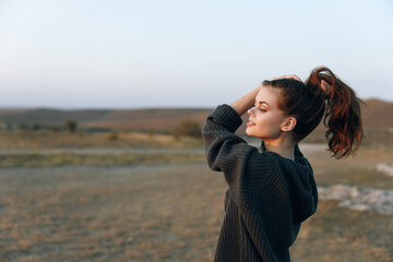 Serene young woman with ponytail standing in open field, gazing up at the vast blue sky