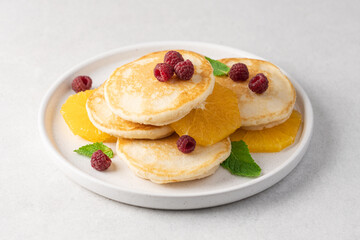 Pancakes with orange and raspberries in plate top view on white background with copy space