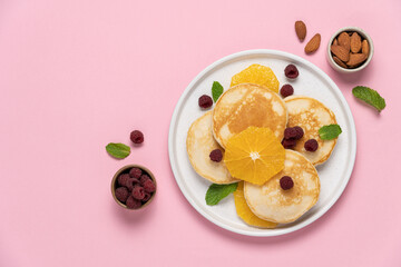 Pancakes with orange and raspberries in plate top view on pink background with copy space. Morning traditional breakfast