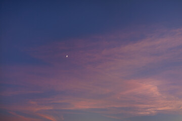 A crescent moon embellishes the sky at dusk, dotting the fiery hues of purple and pink with its bright white figure.