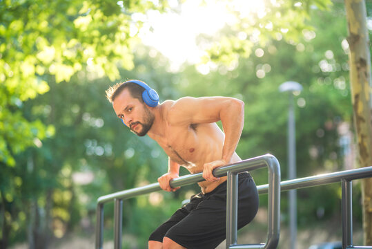 Young man wearing headphones doing dips on parallel bars in a park