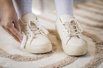 Person cleaning beige sneakers with cloth on carpet