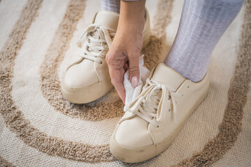 Naklejka premium Person cleaning beige sneakers with cloth on carpet