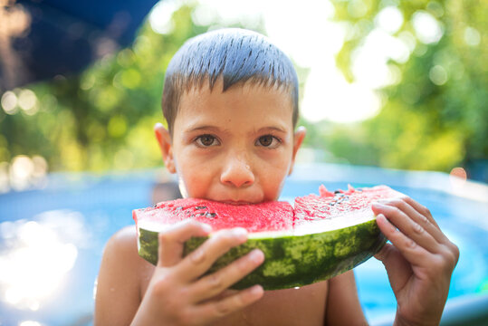 Boy eating watermelon by the swimming pool