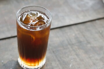 A glass of iced tea with ice cube on wooden table
