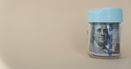 Dollar bills in a glass jar on a yellow background. The concept of saving money