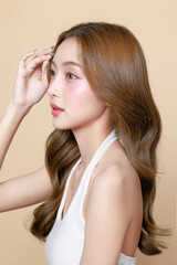 Fototapeta premium Young Asian beauty woman curly long hair with korean makeup style touch her face and perfect skin on isolated beige background. Facial treatment, Cosmetology, plastic surgery.