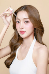 Obraz premium Young Asian beauty woman curly long hair with korean makeup style on face and using pipette to apply serum on skin on isolated beige background. Facial treatment, Cosmetology, plastic surgery.